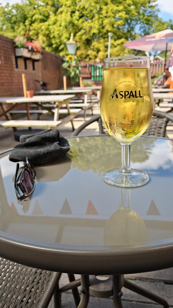 Glass of Aspall cider glistening in the sunshine with sunglasses on the picnic bench in the beer garden