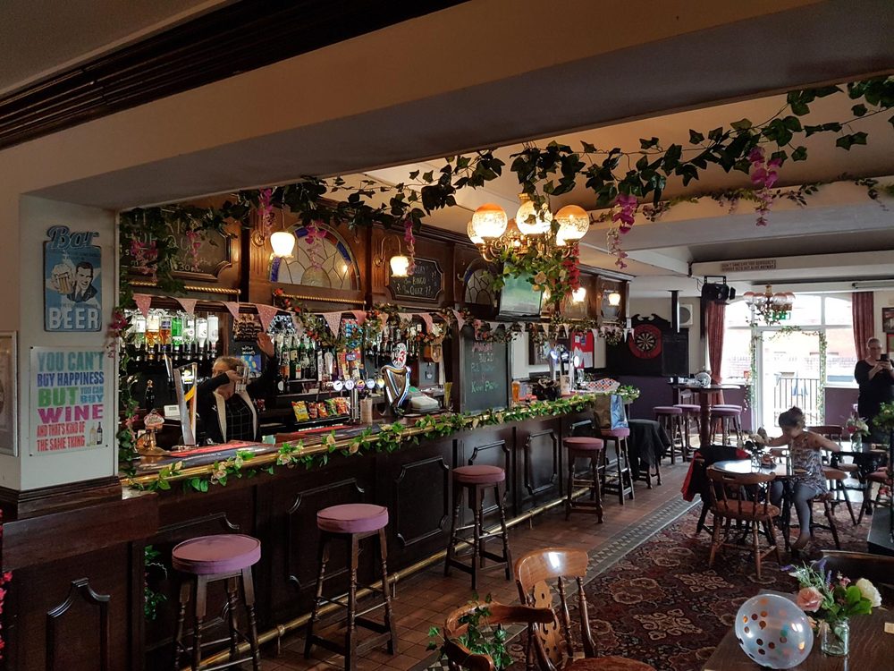 Bar interior with wooden stools, ivy decorations trailing along the ceiling, beer signs, and stained glass panels