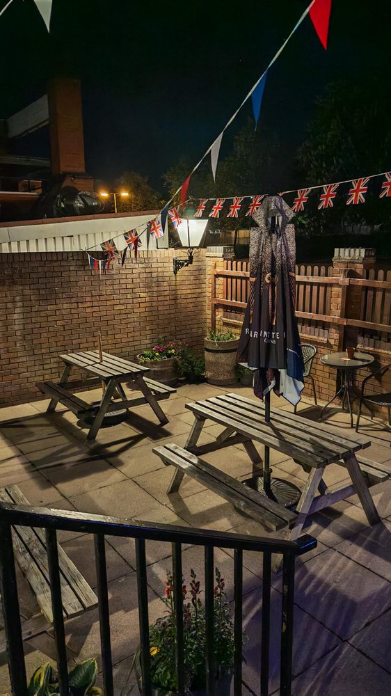 Beer garden at night with Union Jack bunting strung between posts and warm lighting from the pub