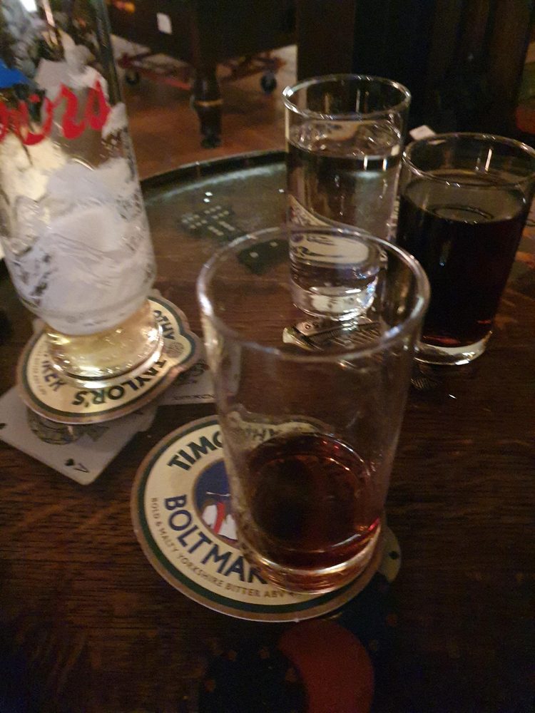 Dominoes spread across a wooden table with pint glasses and Timothy Taylor Boltmaker beer mats