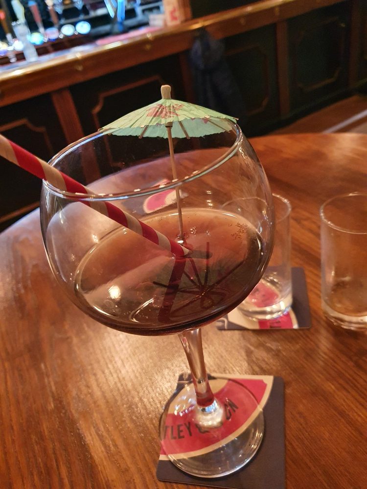 Colourful gin cocktail served with a paper umbrella and stripy straw at the bar