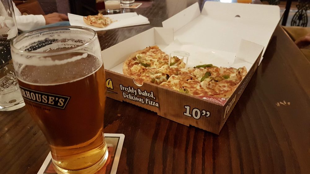 Pint of ale alongside a takeaway pizza box on a pub table