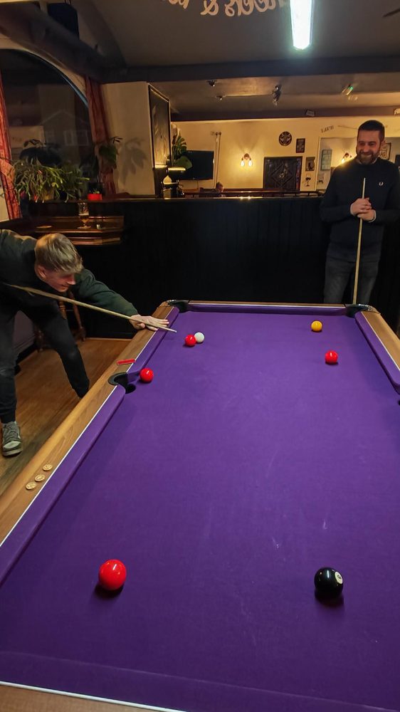Two people playing pool on the purple-felt pool table