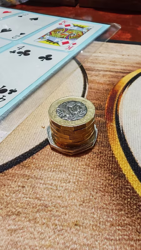 Stack of pound coins on the bar next to playing cards after a quiz night win
